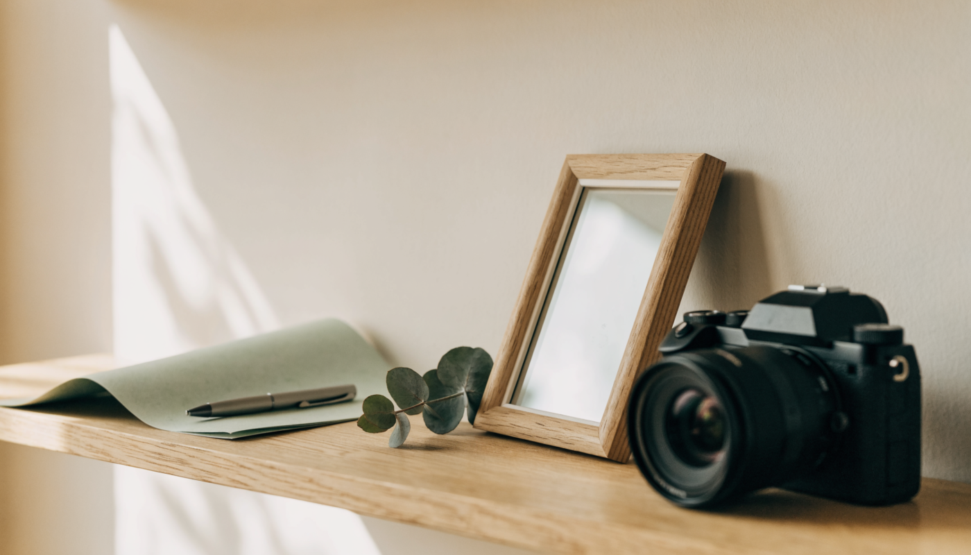 Camera, empty wooden frame and notepad on a dry oak shelf in soft morning light